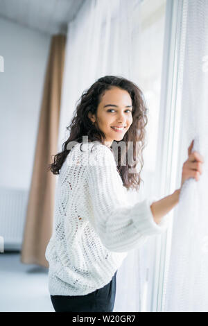 people and hope concept - close up of happy woman opening window curtains Stock Photo