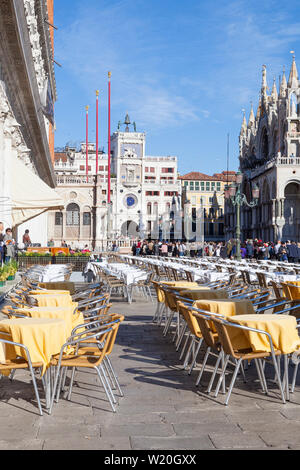 Tables laid ready for lunch in Piazetta San Marco, Venice, Veneto, Italy  with a view to the Clock Tower and Basilica With  crowds of tourists sightse Stock Photo