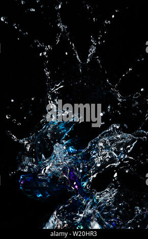 A piece of coloured glass splashes in water against a black background. Stock Photo