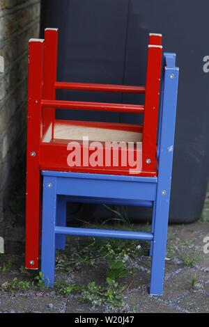 colour image showing two similar wooden chairs, one painted red and the other painted blue stacked onto each other in a neat manner Stock Photo