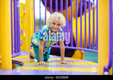 Child playing on outdoor playground. Kids play on school or kindergarten yard. Active kid on colorful slide and swing. Healthy summer activity for chi Stock Photo