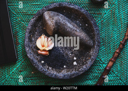 picture of a granite mortar and pestle on a green surface, fresh garlic lies inside the pestle Stock Photo