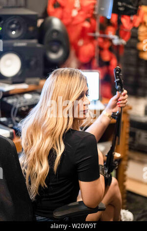 Music recording session in modern music studio. The equipment including violin, keyboards, sound speakers and keyboards. Blonde woman musician. Stock Photo