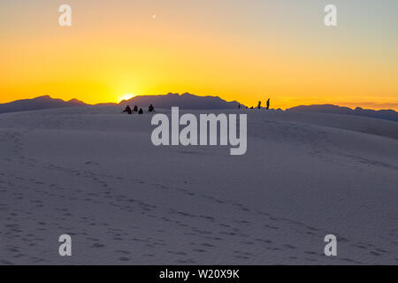 Tourists Watching A Desert Sunset. Tourists stand on top of a sand dune admiring the sunset horizon of the White Sands in New Mexico. Stock Photo