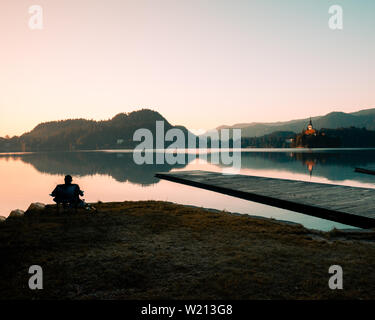 Old fisherman fishing on lake Bled on a sunny spring day during sunrise Stock Photo