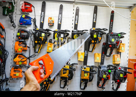 Chelyabinsk Region, Russia - JUNE 2019. Hand saw in hand against the background of a rack with chainsaws. Building tool on store shelves of various ma Stock Photo