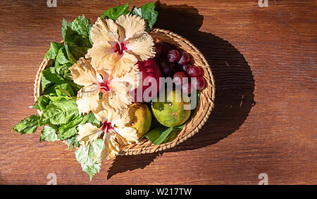 Apple, Orange and grape in weave bamboo baskets with floral decorations on wooden table. Stock Photo