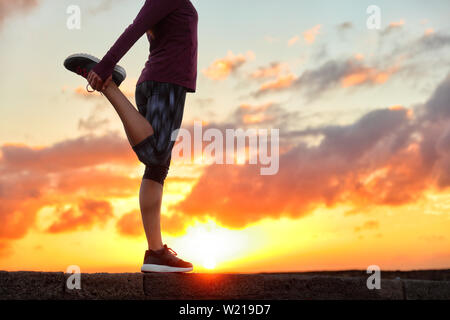 Running runner woman stretching leg muscle preparing for sunset trail run in outdoor summer nature. Female athlete lower body crop of feet doing legs stretches getting ready for cardio warmup. Stock Photo
