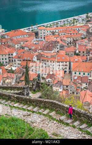 Little girl in pink waterproof jacket walking down on the stony trail and steps leading to the Kotor fortress above Kotor town, Montenegro Stock Photo