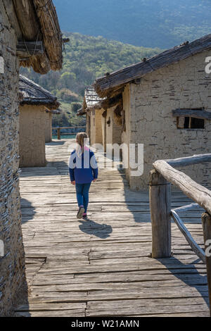 Little Caucasian girl walking among mud and straw houses in the Bay of the bones museum on water, authentic reconstruction of the pile dwelling settle Stock Photo