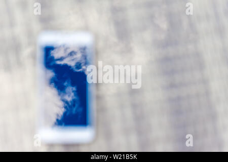 Reflection of blue sky with clouds in the phone-smartphone, which lies on a bright wicker table against the background. Blur and abstraction Stock Photo