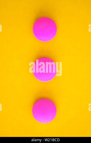 Composition of three pink round pills on a yellow background. Flat lay. Copy space. Trend Close-up. Stock Photo