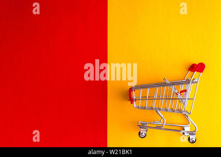 On a yellow-red background, a grocery cart-basket and a question mark. Flat lay, Top view, copy space. Concept, choice of shopping, reasonable and eco Stock Photo