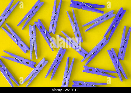 Wooden lilac-purple clothespins scattered on a yellow background. View from above. Copy space. Flat lay. The concept is natural, eco-friendly. Stock Photo