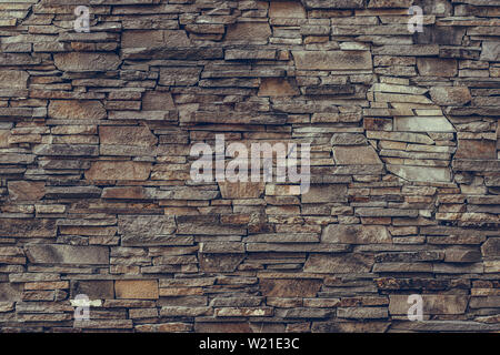 Natural stone wall texture with stacked brown and grey slate slabs, rustic rock facade background for architectural and decorative design. Stock Photo