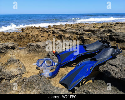 Blue fins and mask for snorkeling, diving lie on the sea shore with waves and blue sky on background Stock Photo