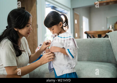 kindergarten student wearing school uniform helped by her mom in the morning. back to school preparation Stock Photo