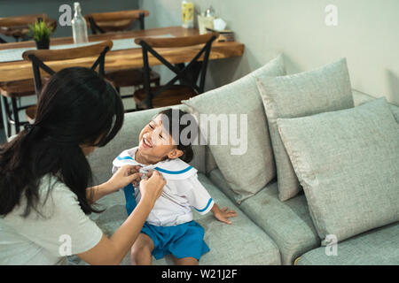 kindergarten student wearing school uniform helped by her mom in the morning. back to school preparation Stock Photo