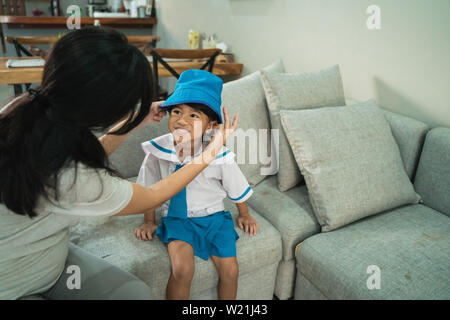 kindergarten student wearing school uniform helped by her mom in the morning. back to school preparation Stock Photo