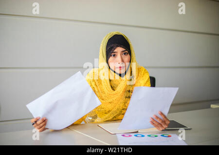 Muslim businesswomen analysis documents on office table and have graph financial diagram working in the background Stock Photo