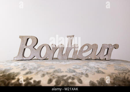 Happiness, word carved in wood and placed on a gray damask fabric (Bonheur is happiness written in French) Stock Photo
