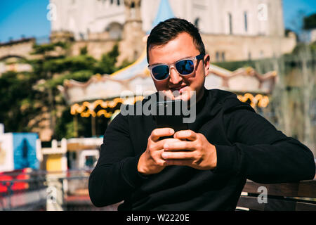 Young handsome man in sunglasses use phone while sitting on the bench. Stock Photo