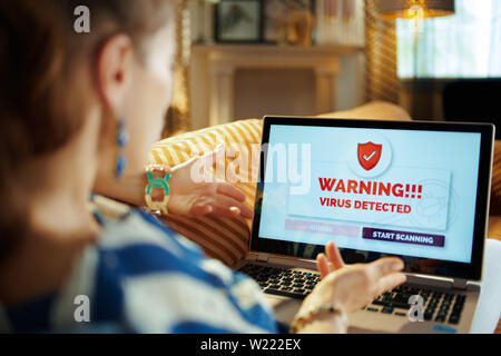Over shoulder shot of furious young housewife laying on sofa in the modern living room in sunnny hot summer day having virus on a computer. Stock Photo