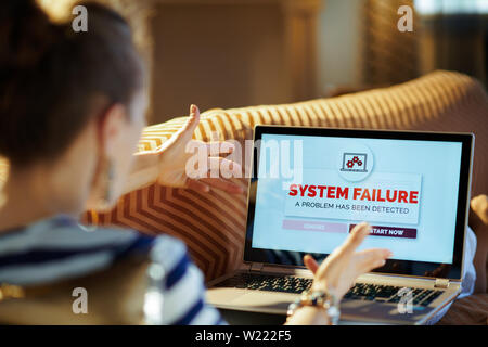 Over shoulder shot of angry modern woman laying on sofa at modern home in sunnny hot summer day looking at computer error screen on a laptop. Stock Photo