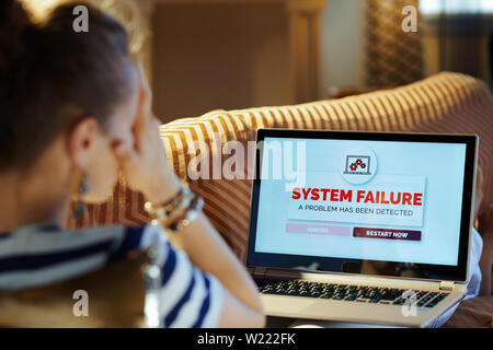 Over shoulder shot of stressed modern housewife laying on sofa in the modern living room in sunnny hot summer day experiencing computer fault on lapto Stock Photo