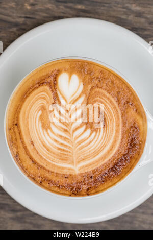 Cup of cappuccino coffee with beautiful latte art served on wooden table. Stock Photo