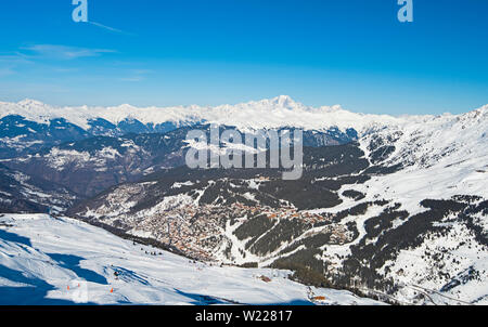 Panoramic view across snow covered alpine mountain range in alps on blue sky background with mountain village Stock Photo