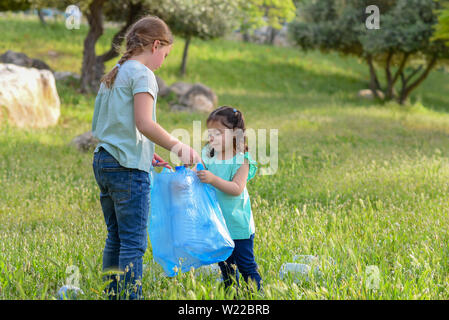 Plastic pollution on land. Polluted park, environmental rubish. Children volunteers with garbage bags cleaning up garbage outdoors.Happy child holding package for plastic bottles. Stock Photo