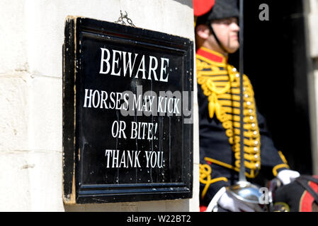 London, England, UK. Member of the King's Troop, Royal Horse Artillery, on duty outside Horse Guards in Whitehall beside warning sign Stock Photo