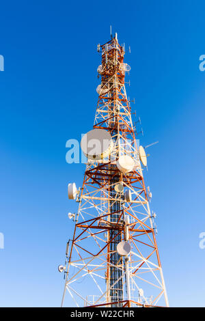 Large telecommunications mast on top of a mountain painted red and white, and containing many microwave dishes, mobile phone antennae, yagis dipoles Stock Photo