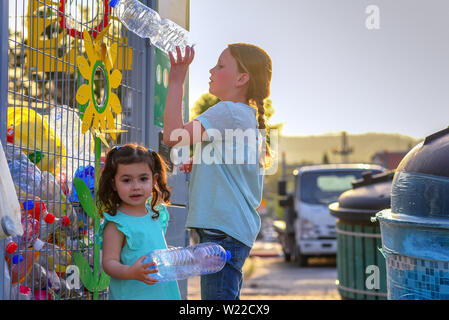 Little Girls Recycling Plastic Water Bottles in Yellow Metal Recycling Cage. Children Puts Plastic Waste in Recycling Bins in Street of City. Stock Photo