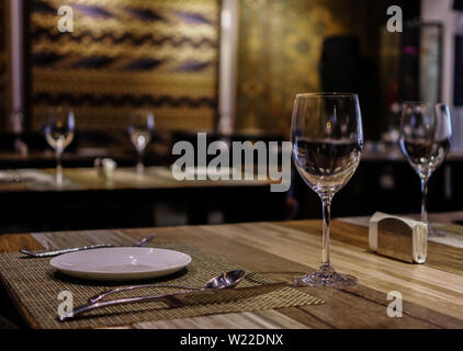 Empty wineglasses and tableware on wooden table in restaurant with silk rug carpets on the wall Stock Photo