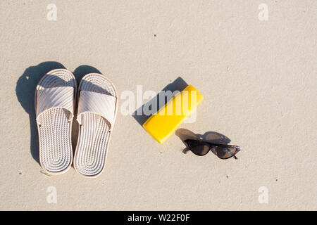 Rest on the beach: slippers, protective cream and sunglasses on clean sand. Top view of acessories for seaside holidays or summer vacation Stock Photo