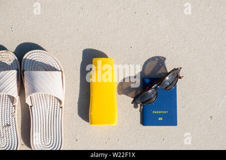 Rest on the beach: slippers, protective cream and sunglasses on clean sand. Acessories for seaside holidays or summer vacation and biometric passport Stock Photo