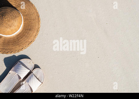 Summer vacation concept: beach slippers and a hat on clean sand. Top view of acessories for seaside holidays with natural copy space resembling seasho Stock Photo