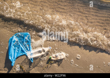 Plastic bag and bottles on the beach, seashore and water pollution concept. Trash (empty food package) thrown away at the seaside, top view with waves Stock Photo