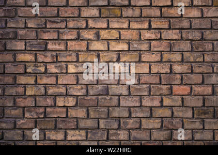 Wall made from red and sometimes colorful bricks of regular shapes and random distribution slotting together precisely. Closeup architecture. Stock Photo