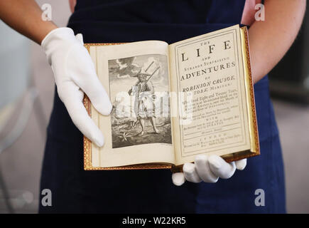 A Sotheby's employee handles a first edition of 'Robinson Crusoe' by Daniel Defoe which will be included in Sotheby's upcoming English literature, history, children's books, and illustrations auction. Stock Photo