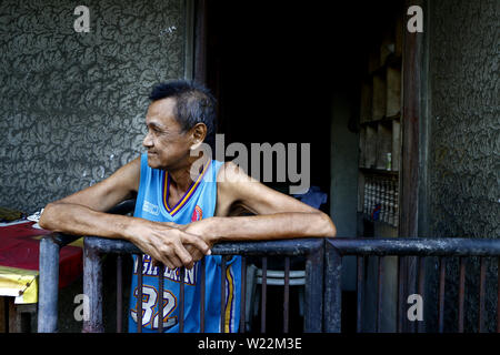 ANTIPOLO CITY, PHILIPPINES – JULY 3, 2019: A mature Filipino man stands outside the front of his home and looks on as if waiting for someone. Stock Photo
