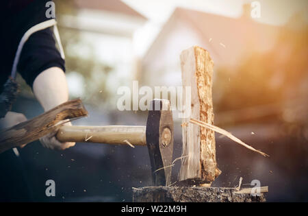 A man in the village , dressed in a black jacket, chopping with an ax a log, which from the blow split into splinters Stock Photo