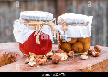 Glass jars containing redcurrant jam and cherries in syrup served on a rustic natural shaped wood table. Stock Photo