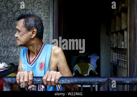 ANTIPOLO CITY, PHILIPPINES – JULY 3, 2019: A mature Filipino man stands outside the front of his home and looks on as if waiting for someone. Stock Photo