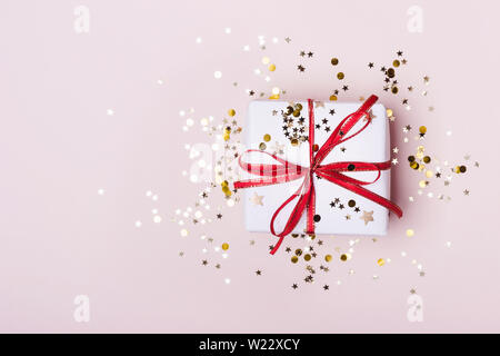 Gift box with red bow and sparkles confetti on pink pastel background. Festive concept. Stock Photo