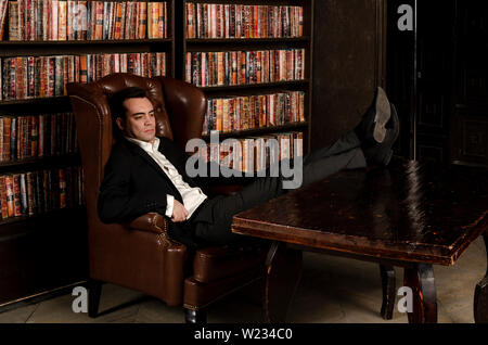 Handsome and attractive male in library full of books, looking sophisticated, strong, serious. Like good looking italian mafia, writer or businessman Stock Photo