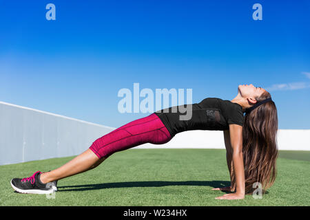 Yoga fitness woman stretching body in upward plank pose doing reverse planking exercise on outdoor grass park. Sport woman strength training her core body with bodyweight flexibility exercises. Stock Photo