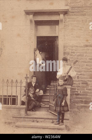 Victorian September 1889 Photograph of a Fashionable Family Posing at The Entrance To 'Raglan House', Borth, Wales. One of The Ladies Sat on The Wall Playing The Banjo Ukulele. Stock Photo